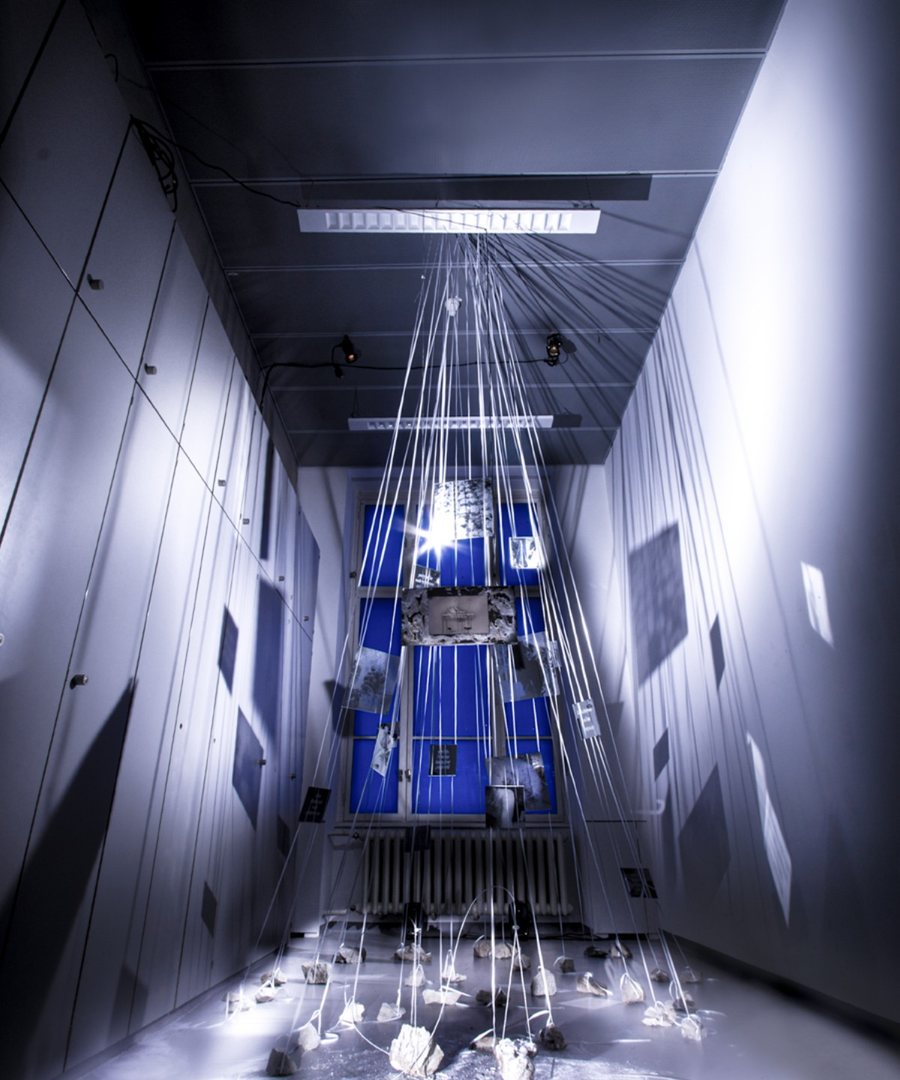Tall installation view with suspended elements in a blue-lit space.