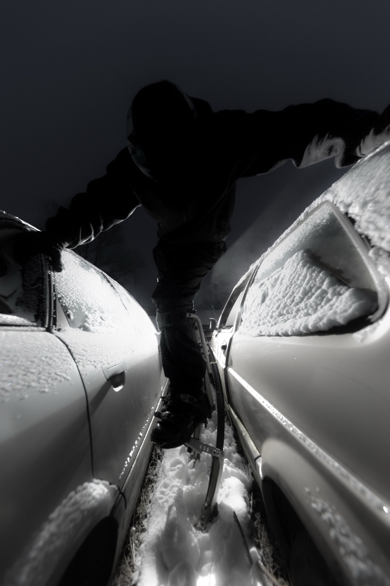 Masked figure standing between snow-covered cars.