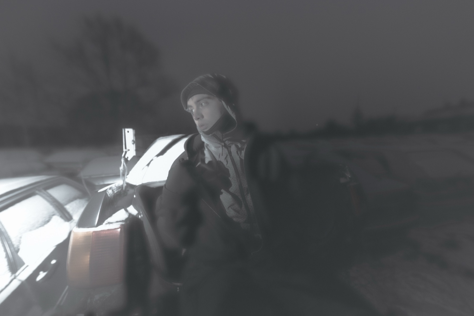 Masked figure beside a car in foggy light.
