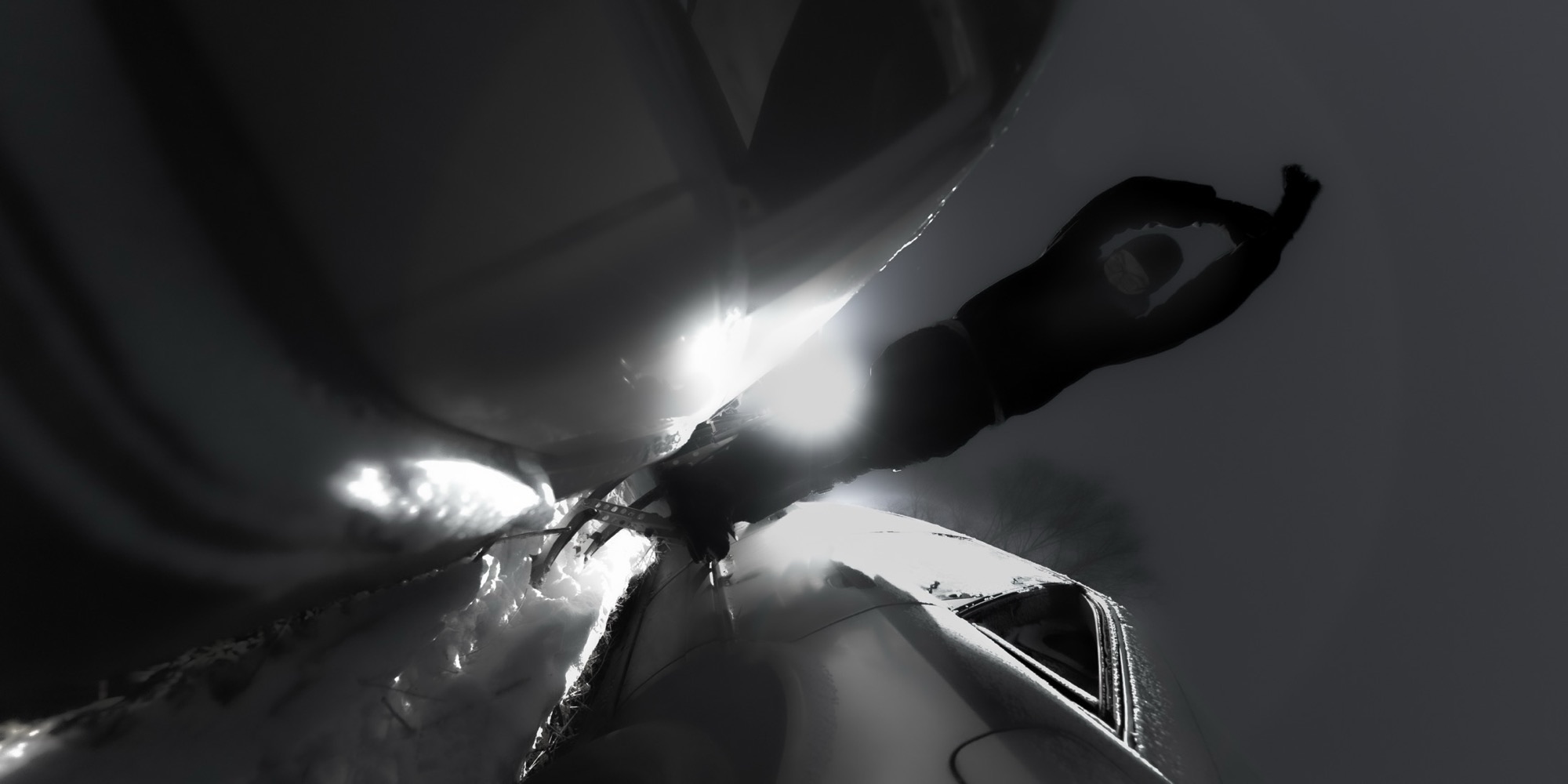 Masked figure between cars with bright headlights.