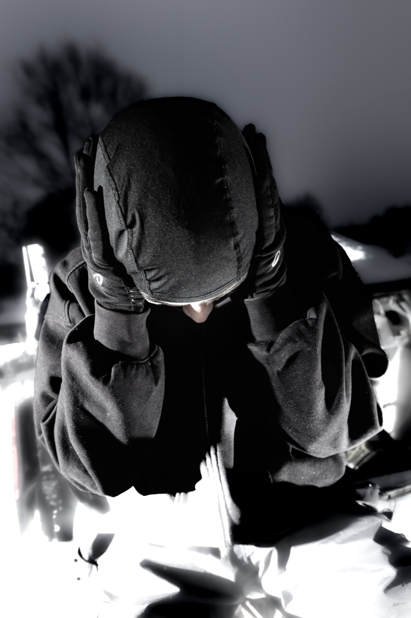 Masked figure holding their head in bright car light.